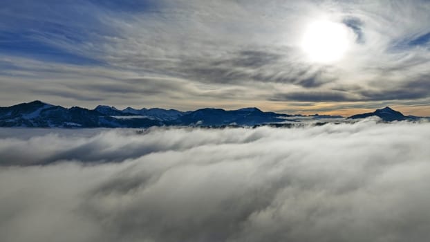Drone shot in winter with fog in the valley and sun in the mountains