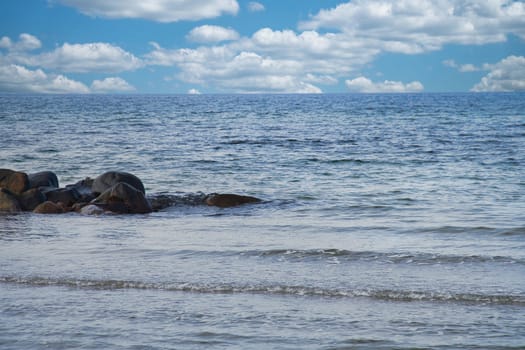 By the sea of the Baltic Sea. Stone groynes reach into the blue water. White clouds in the sky. Landscape shot of the coast.