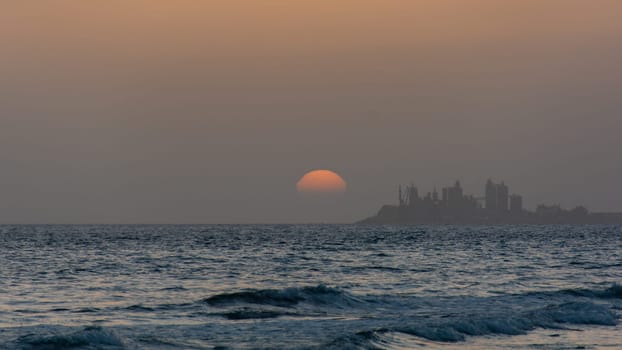 Sunset over the sea with a city in silhouette in the background