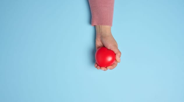 Woman's hand holding a red heart on a blue background