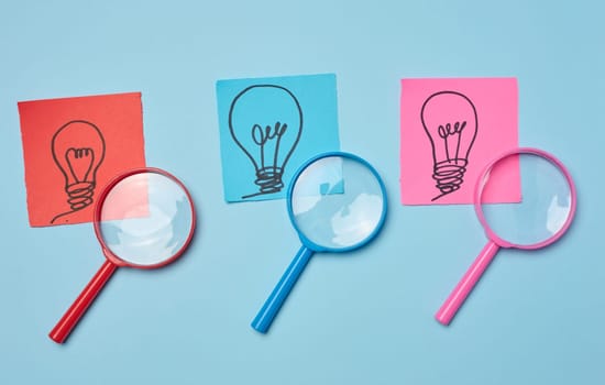 Drawn light bulbs on sheets of paper and a plastic magnifying glass, the concept of searching for new ideas