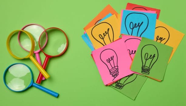 Drawn light bulbs on sheets of paper and a plastic magnifying glass, the concept of searching for new ideas.