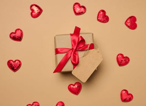 Box tied with a red ribbon and small hearts on a beige background, top view