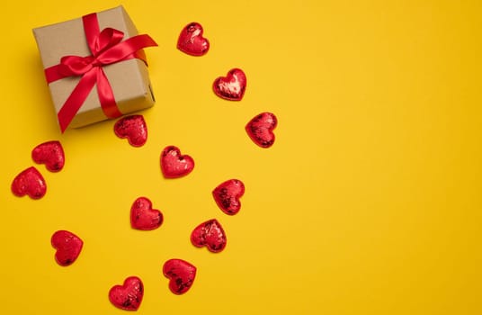 Box tied with a red ribbon and small hearts on a yellow background, top view