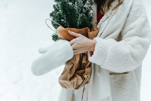 Close up photo of female hands put on wool mittens outdoors, holding pine bouquet.