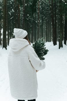Blonde woman wears white fur coat and knitted hat posing with fir tree in winter forest, back view