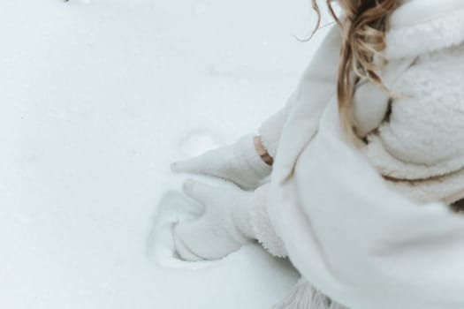 Woman's hands in white mittens taking snow, making snowball.