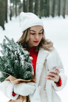 Young woman in a snowy forest with smartphone chatting online outdoors in the wild