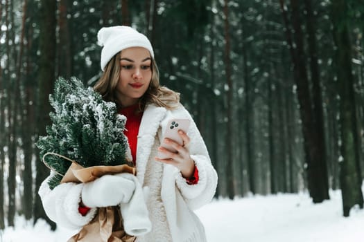 Young woman in a snowy forest with smartphone chatting online outdoors in the wild