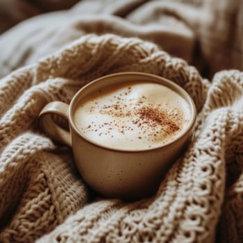 A cozy cup of cappuccino with cinnamon, nestled in a soft, knitted blanket. Perfect for warm, relaxing moments
