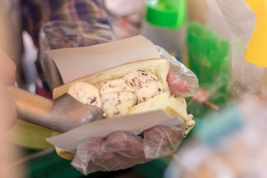 Hands of a male merchant scoop vanilla chocolate chip ice cream into bread and toppings for customers