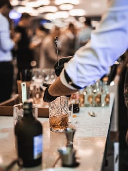 Expert barman is making cocktail at business banquet event in hotel conference center. Blurred businesspeople at banquet event business meeting event in the background.