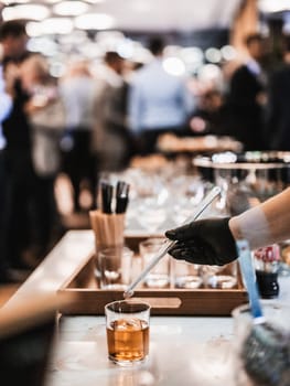 Expert barman is making cocktail at business banquet event in hotel conference center. Blurred businesspeople at banquet event business meeting event in the background.