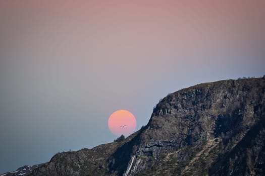 Westcap in Norway. Mountain that reaches into the fjord. Moon shining red behind the mountain. Landscape shot from Scandinavia