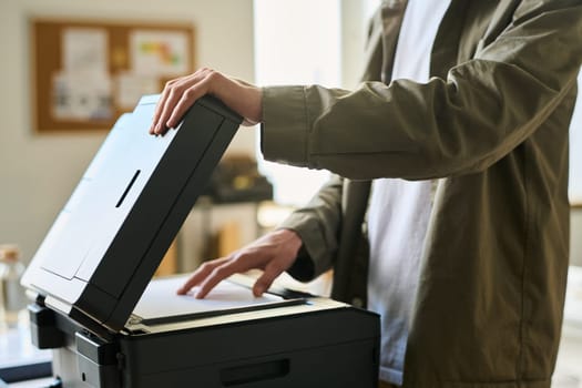 Cropped shot of young businessman putting paper on copier screen of xerox machine to make some copies of financial documents
