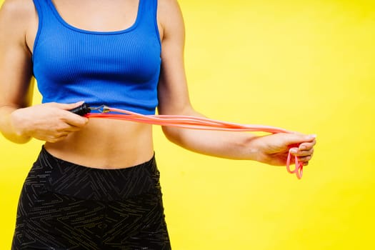 Fit female athlete with jumping with rope during fitness training against yellow background