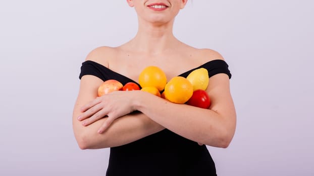 A female holding an apples, lemons, oranges in different arms isolated on grey background.