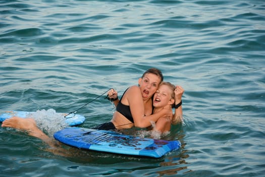 Two children have fun in the sea water, with swimming boards and funny facial expressions