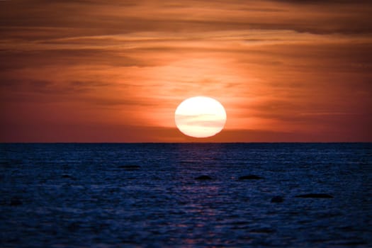 Sunset over the Baltic Sea. The red sun sinks into the sea. Evening atmosphere on the coast. Landscape photograph in northern Germany