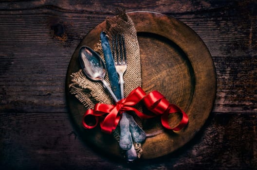 Valentines dinner setting with vintage silverware, dinner plate and red ribbon on wooden table. Valentine day background frame for special romantic dining celebration. Top view.