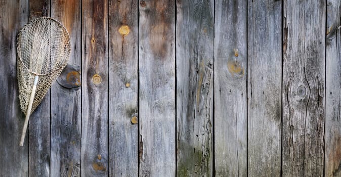 Fishing concept. Old fisherman equipment on vintage wooden background with copyspace. Landing net hooked on rustic board.