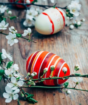 Closeup of colorful painted easter eggs and cherry blossom branch decor on vintage wooden table. Traditional seasonal holiday still life. Easter celebrate and spring concept.