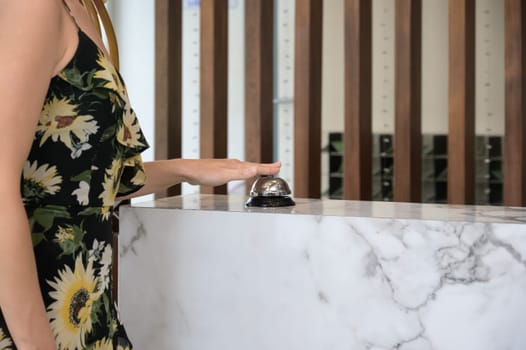 Hotel reception. Hand of caucasian woman guest ringing on service bell at hotel check in counter