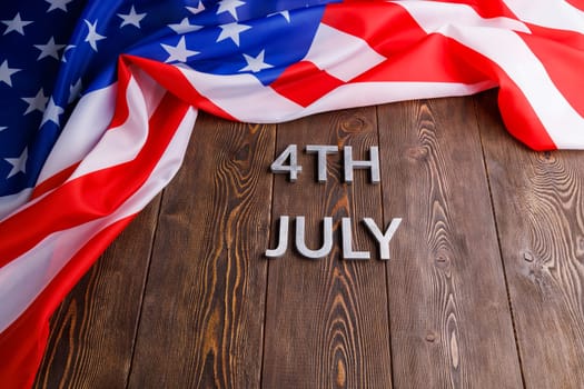 the words 4th july and crumpled usa flag on flat textured wooden surface background.