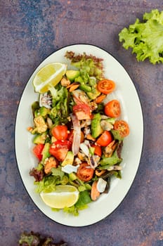 Delicious salad with fresh vegetables and seafood on a plate. Close up.
