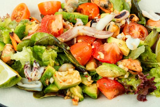 Delicious salad with fresh vegetables and seafood on a plate. Close up.