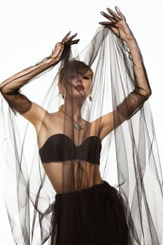 Beautiful woman in a transparent black skirt, bodice and neck decoration posing on a white background.