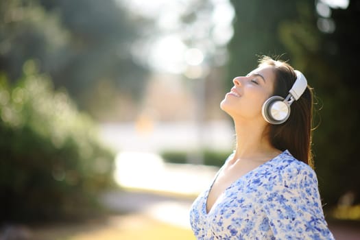 Side view portrait of a happy woman listening audiobook meditating with headphone in a park