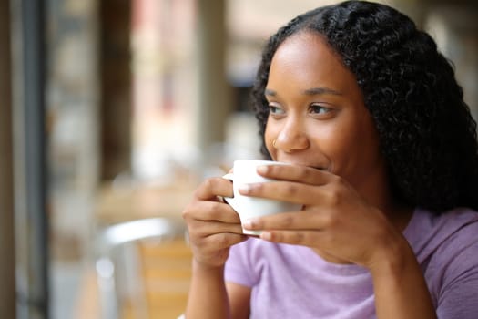 Satisfied black woman drinking coffee looking away in a restaurant terrace