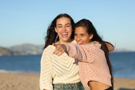 Two funny friends pointing away on the beach at sunset