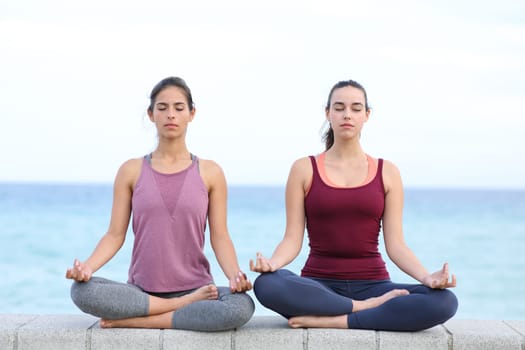 Front view portrait of two friends practicing yoga on the beach
