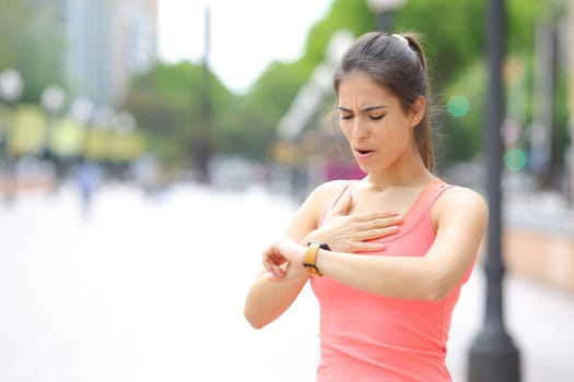 Tired runner checking time on smartwatch after running in the street