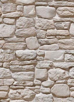 The wall is made of artificial stone in the form of a round beige cobblestone. Texture or background.
