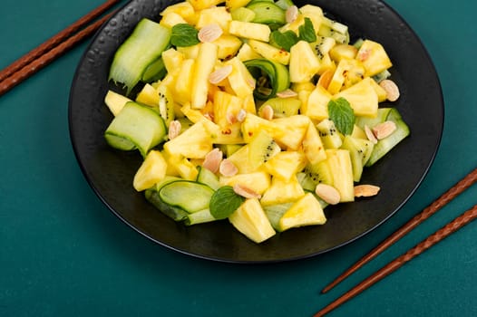Vegan fresh pineapple and cucumber salad. Pineapple salad served on a black plate and chopstick.