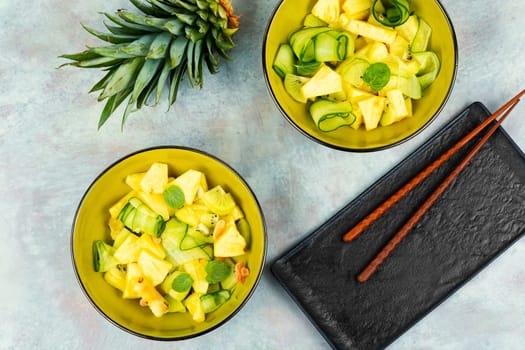 Vegan fresh pineapple and cucumber salad. Pineapple salad served on a black plate and chopstick.
