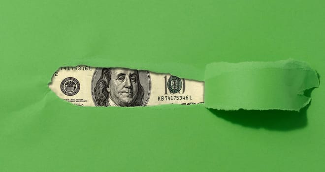 A green sheet of paper with a torn middle and a curled edge, a hundred dollar bill in the hole.