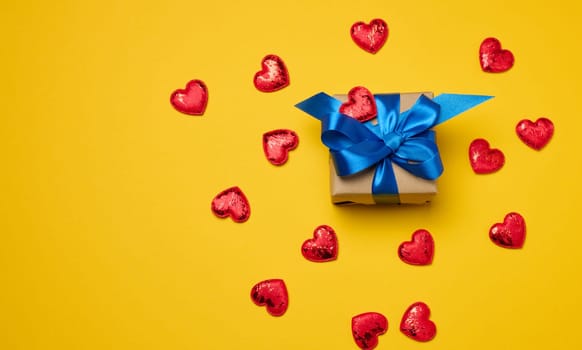 Box tied with a red ribbon and small hearts on a yellow background, top view