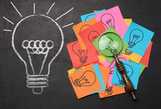 Drawn light bulbs on sheets of paper and a plastic magnifying glass, the concept of searching for new ideas