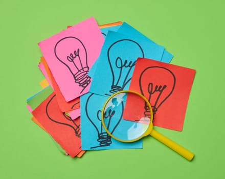 Drawn light bulbs on sheets of paper and a plastic magnifying glass, the concept of searching for new ideas.