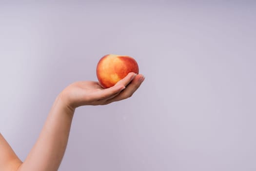 Studio portrait of a happy young woman, smiling, holding ripe nectarines in hands