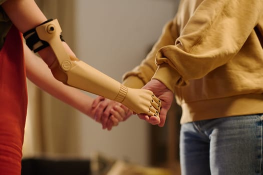 Young woman in pullover and blue jeans holding her daughter with myoelectric arm by hands while standing in front of her