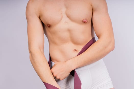 Athlete with muscular body in white panties is doing physical exercises with rubber