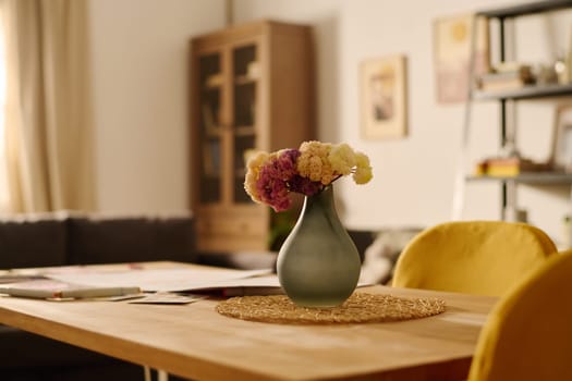 Table with bunch of flowers in grey vase and two yellow chairs standing near by in the center of living room of modern apartment