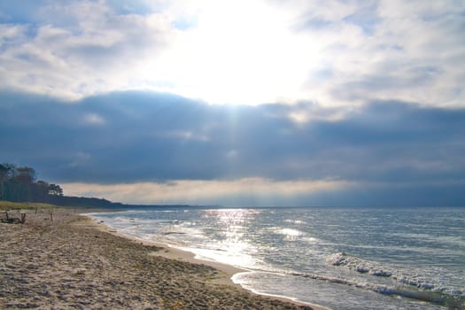 Sunset on the west beach on the Baltic Sea. Waves, beach, cloudy sky and the last rays of sunshine on the coast. Landscape photo