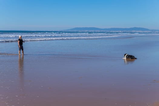 Costa da Caparica: January 21, 2024: Woman playing with her dog at the beach of Costa da Caparica, Portugal