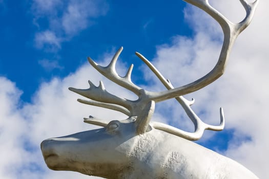 Reindeer statue against the blue sky with white clouds.